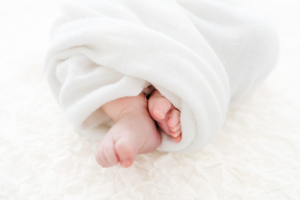 Baby toes peeking from a soft white swaddle during a relaxed baby photography session in Westbury, Wiltshire