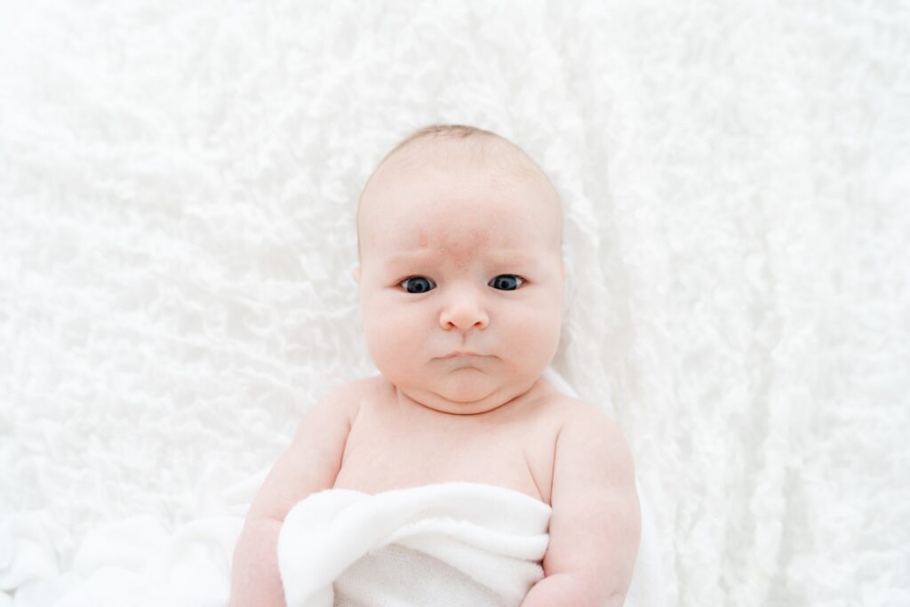 Timeless older baby portrait wrapped in a white swaddle with wide open eyes.